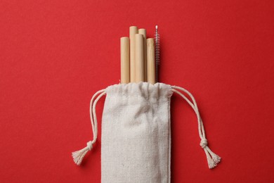 Photo of Bamboo drinking straws and cleaning brush in bag on red background, top view