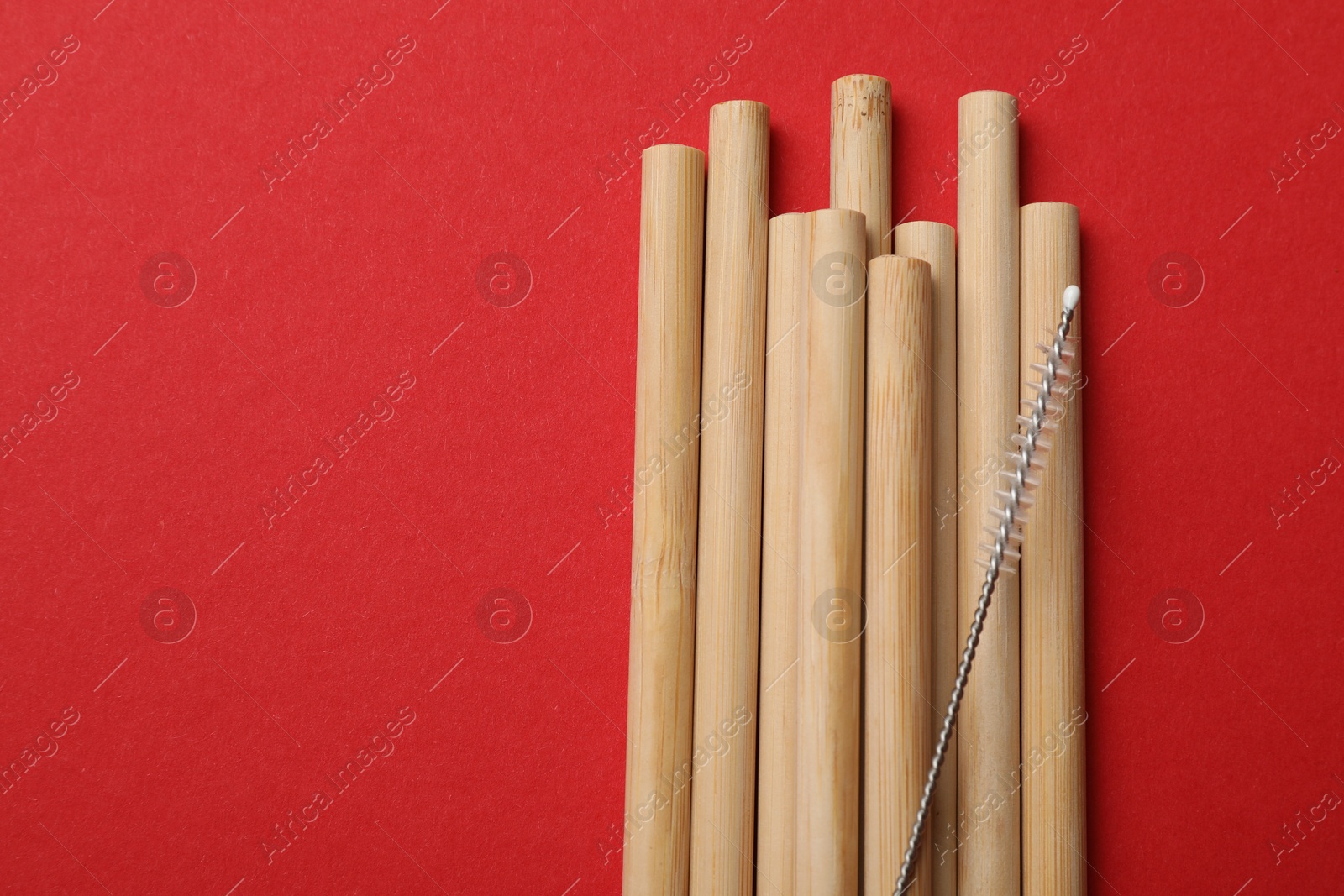 Photo of Bamboo drinking straws and cleaning brush on red background, top view. Space for text