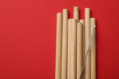 Photo of Bamboo drinking straws and cleaning brush on red background, top view. Space for text