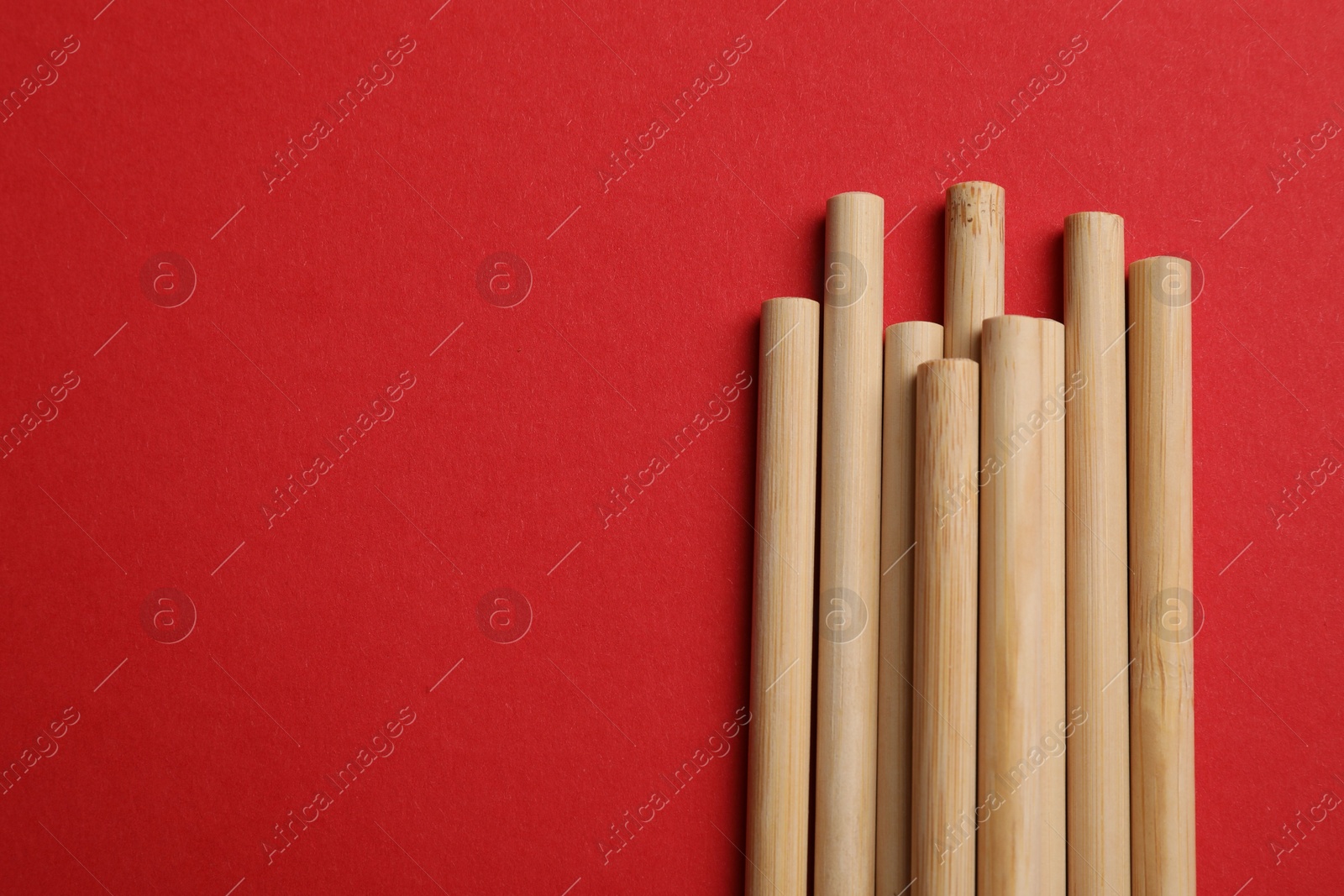 Photo of Bamboo drinking straws on red background, top view. Space for text