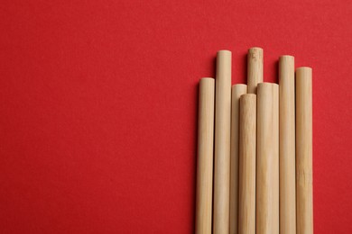 Photo of Bamboo drinking straws on red background, top view. Space for text