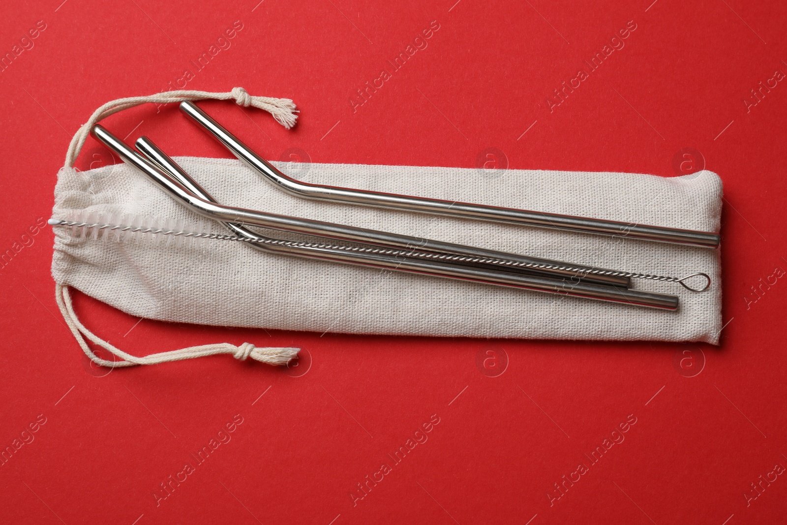 Photo of Metal drinking straws, cleaning brush and bag on red background, top view