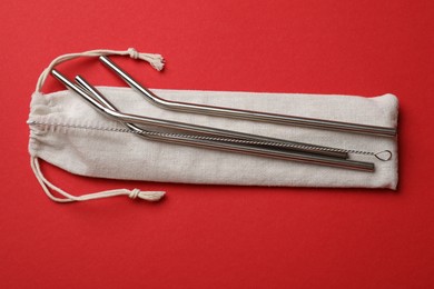 Photo of Metal drinking straws, cleaning brush and bag on red background, top view