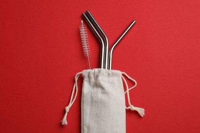 Photo of Metal drinking straws and cleaning brush in bag on red background, top view