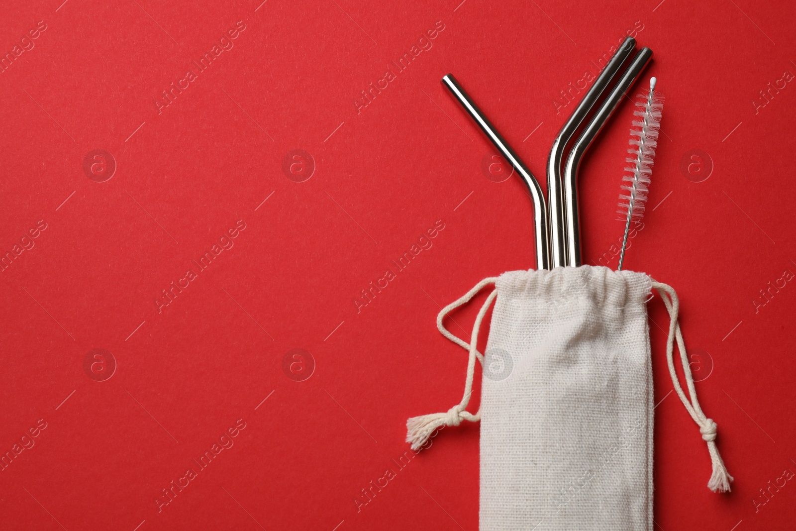 Photo of Metal drinking straws and cleaning brush in bag on red background, top view. Space for text