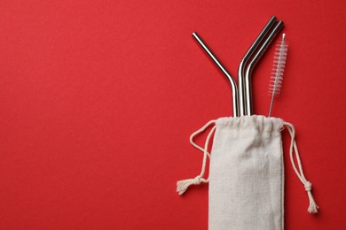 Photo of Metal drinking straws and cleaning brush in bag on red background, top view. Space for text