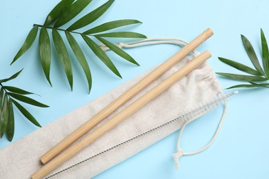 Photo of Bamboo drinking straws, cleaning brush, bag and palm leaves on light blue background, flat lay