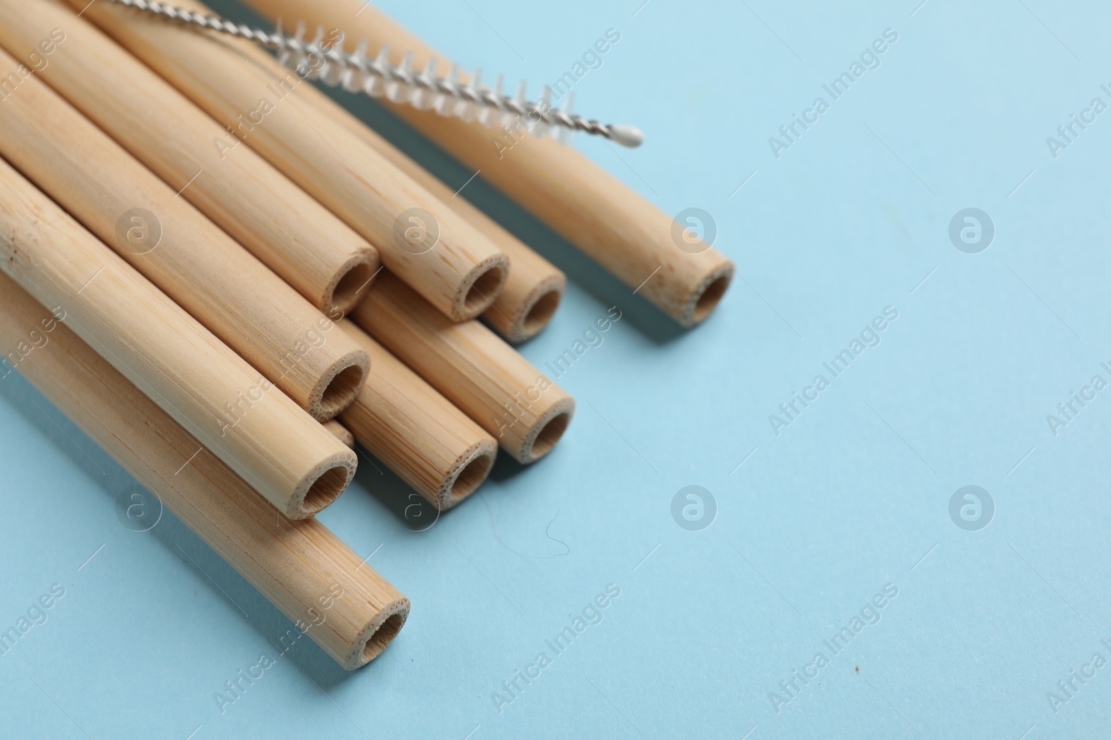 Photo of Bamboo drinking straws and cleaning brush on light blue background, closeup. Space for text