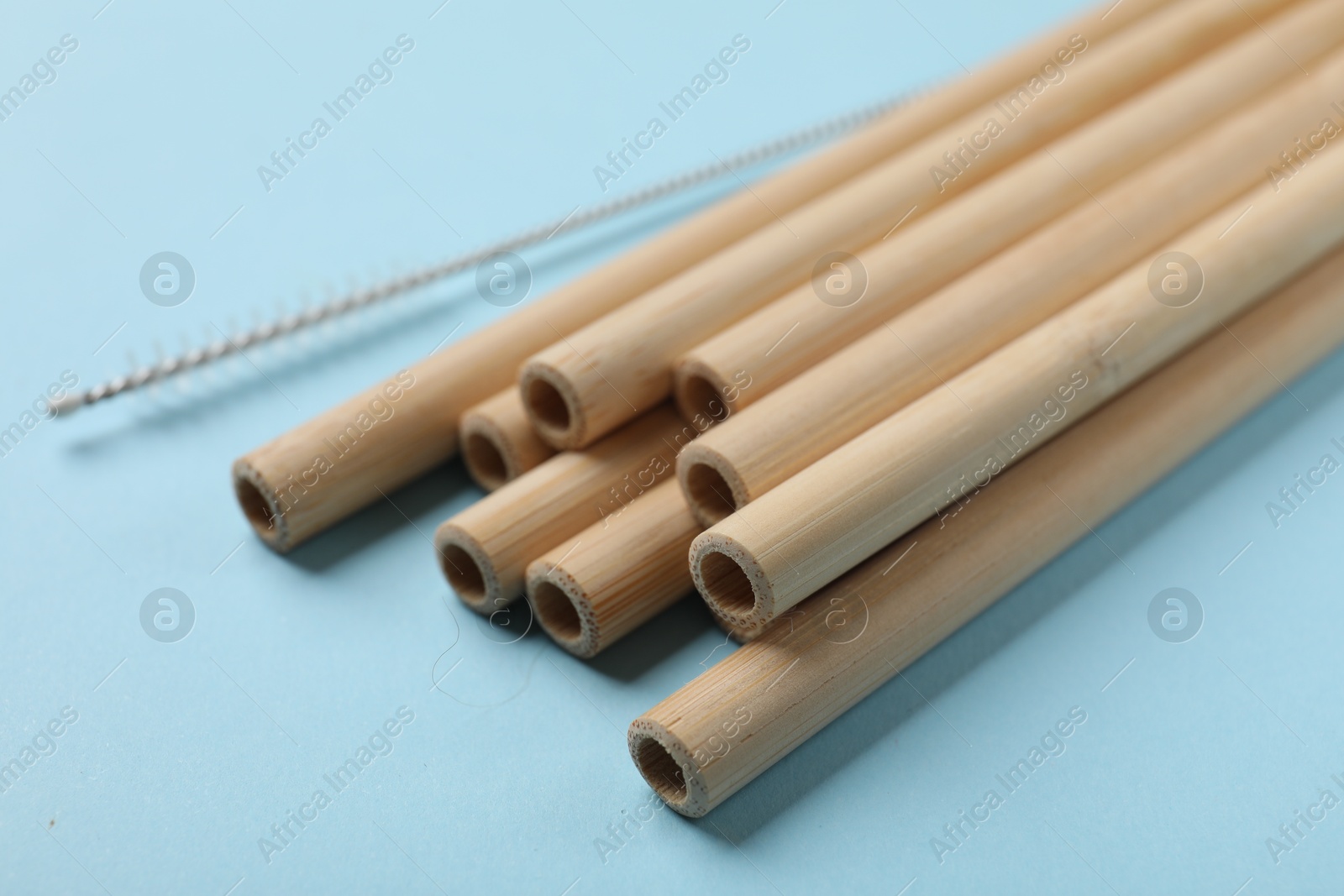 Photo of Bamboo drinking straws and cleaning brush on light blue background, closeup