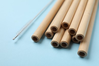 Photo of Bamboo drinking straws and cleaning brush on light blue background, closeup