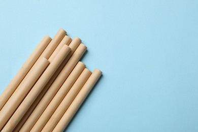 Photo of Bamboo drinking straws on light blue background, top view. Space for text