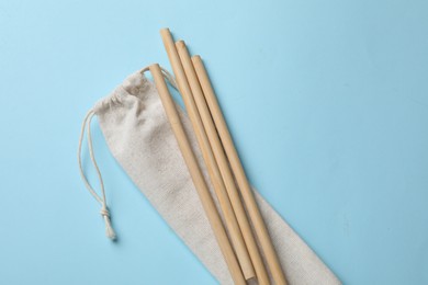 Photo of Bamboo drinking straws and bag on light blue background, top view