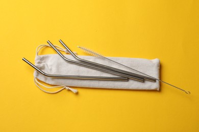 Photo of Metal drinking straws, cleaning brush and bag on yellow background, top view