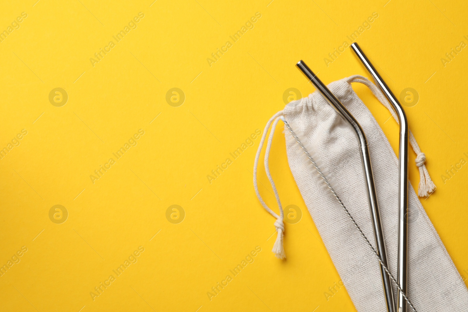 Photo of Metal drinking straws, cleaning brush and bag on yellow background, top view. Space for text