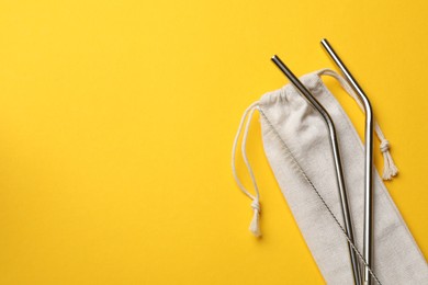 Photo of Metal drinking straws, cleaning brush and bag on yellow background, top view. Space for text