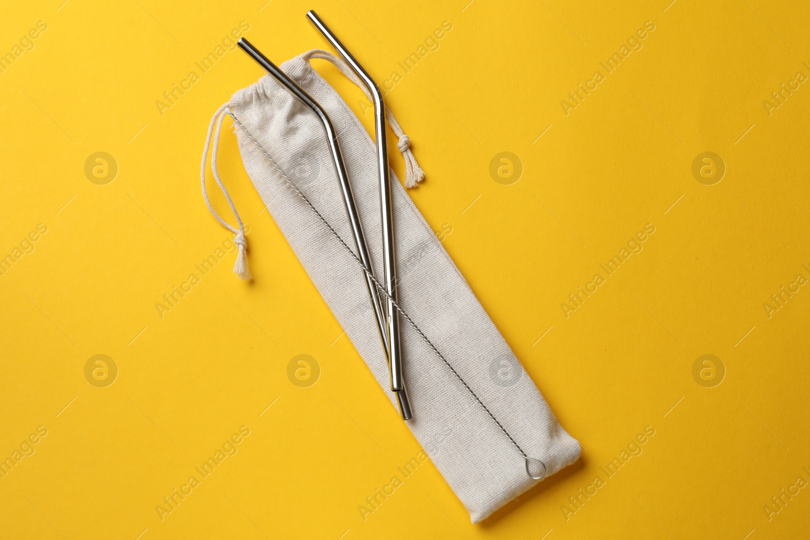 Photo of Metal drinking straws, cleaning brush and bag on yellow background, top view