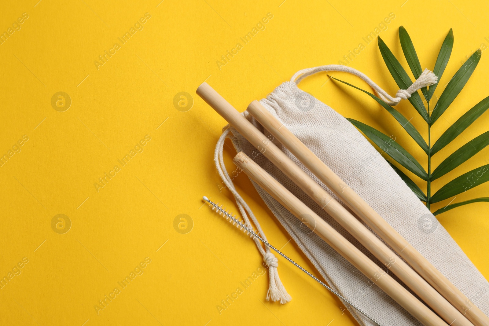 Photo of Bamboo drinking straws, cleaning brush and bag on yellow background, top view. Space for text