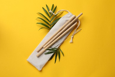 Photo of Bamboo drinking straws, cleaning brush and bag on yellow background, top view