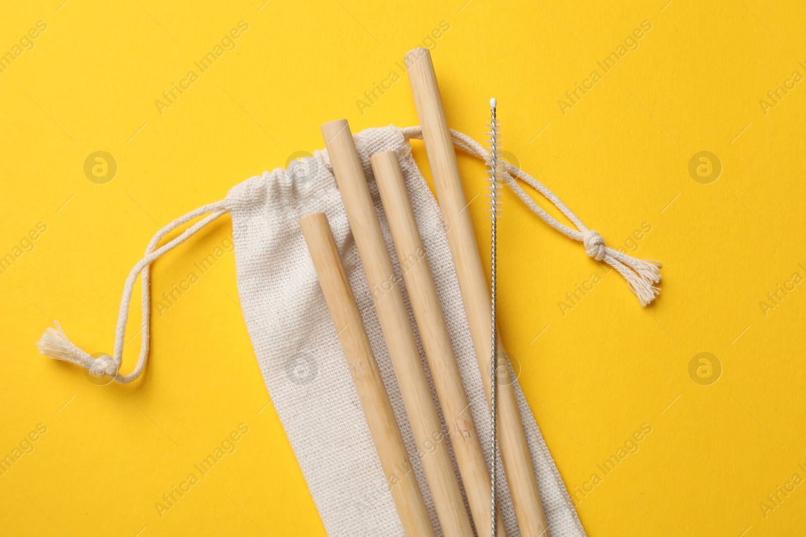 Photo of Bamboo drinking straws, cleaning brush and bag on yellow background, top view