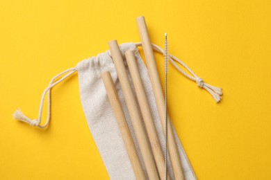 Photo of Bamboo drinking straws, cleaning brush and bag on yellow background, top view