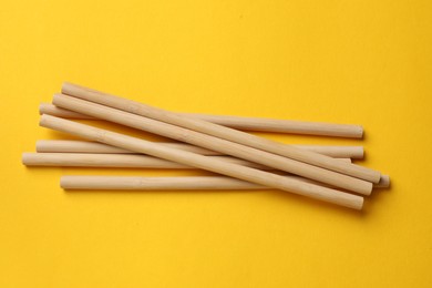 Photo of Bamboo drinking straws on yellow background, top view