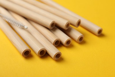 Photo of Bamboo drinking straws and cleaning brush on yellow background, closeup