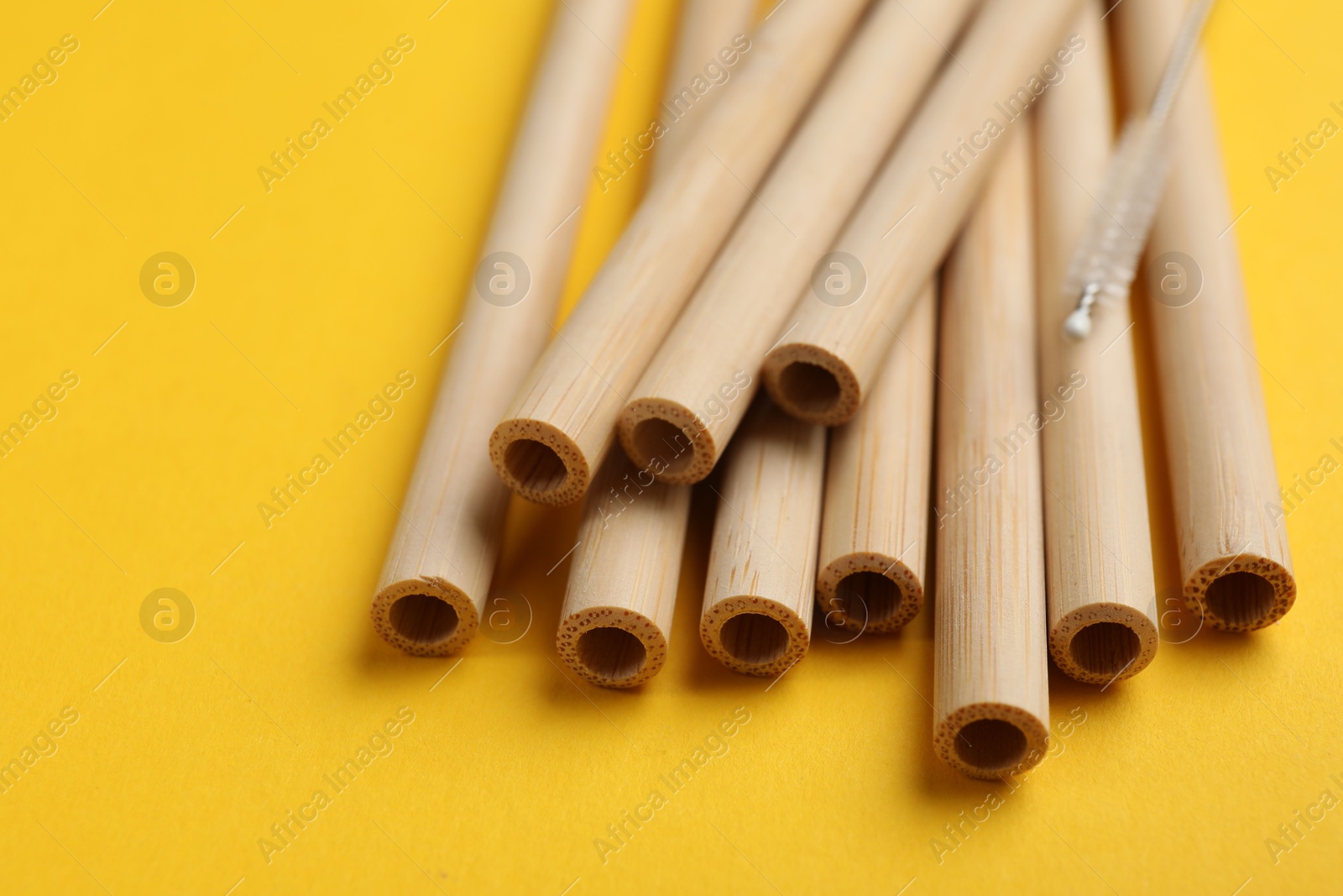 Photo of Bamboo drinking straws and cleaning brush on yellow background, closeup