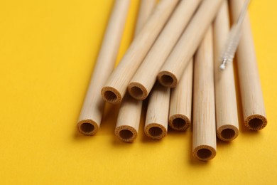 Photo of Bamboo drinking straws and cleaning brush on yellow background, closeup