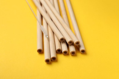 Photo of Bamboo drinking straws and cleaning brush on yellow background, closeup