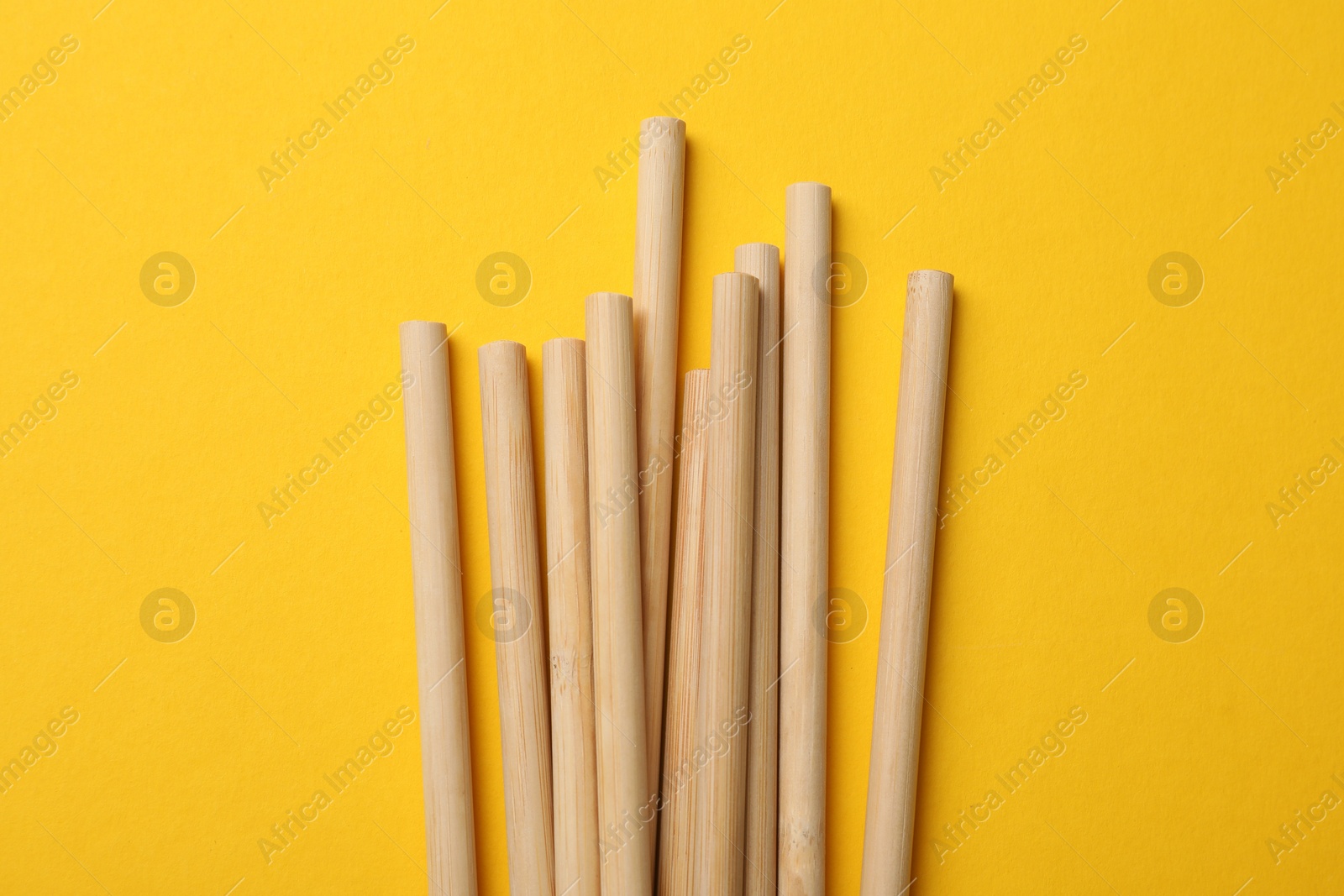 Photo of Bamboo drinking straws on yellow background, top view