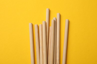 Photo of Bamboo drinking straws on yellow background, top view