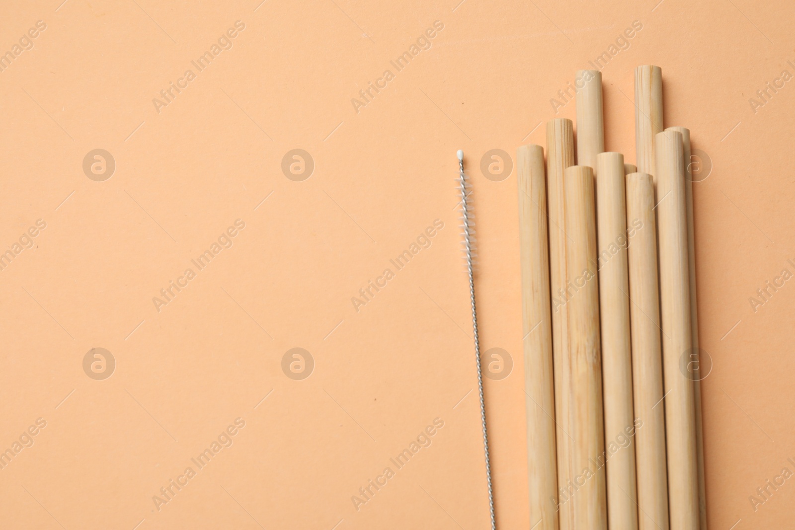 Photo of Bamboo drinking straws and cleaning brush on beige background, top view. Space for text