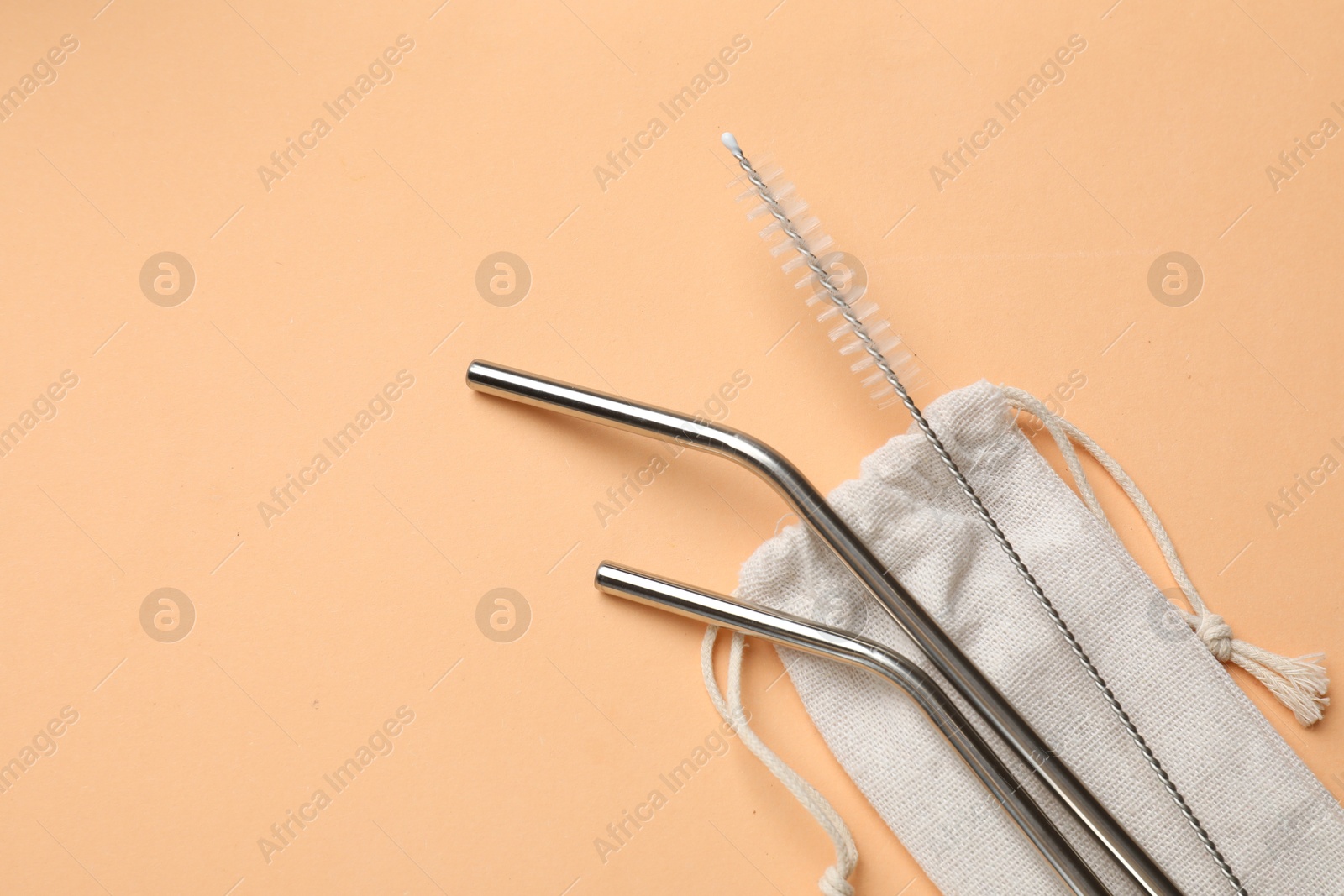 Photo of Metal drinking straws, cleaning brush and bag on beige background, top view. Space for text