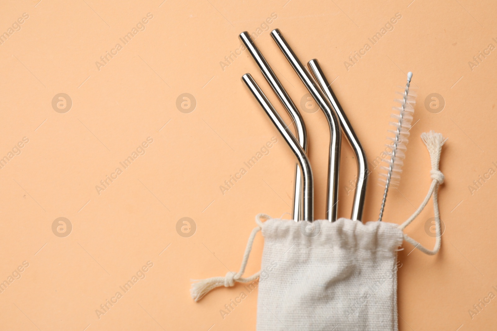 Photo of Metal drinking straws and cleaning brush in bag on beige background, top view. Space for text