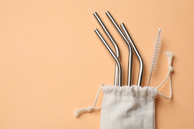 Photo of Metal drinking straws and cleaning brush in bag on beige background, top view. Space for text