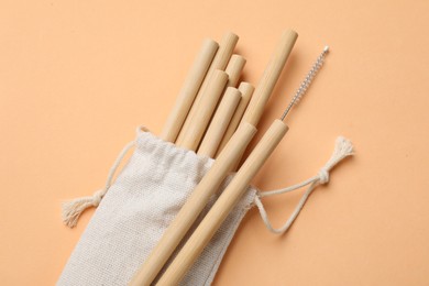 Photo of Bamboo drinking straws and cleaning brush in bag on beige background, top view