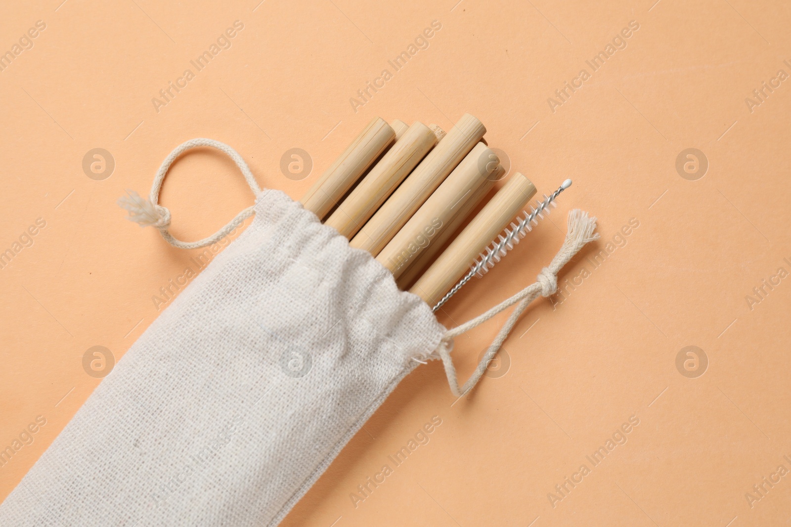 Photo of Bamboo drinking straws and cleaning brush in bag on beige background, top view