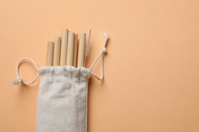 Photo of Bamboo drinking straws and cleaning brush in bag on beige background, top view. Space for text