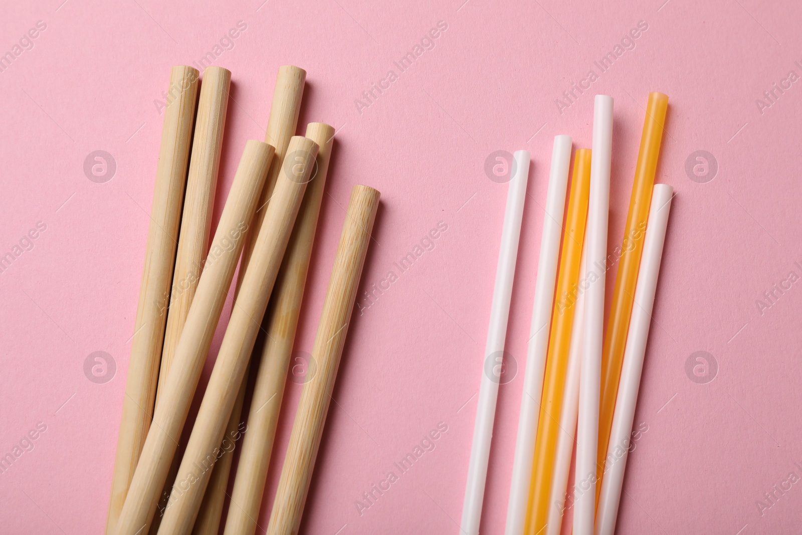 Photo of Plastic and bamboo drinking straws on pink background, flat lay