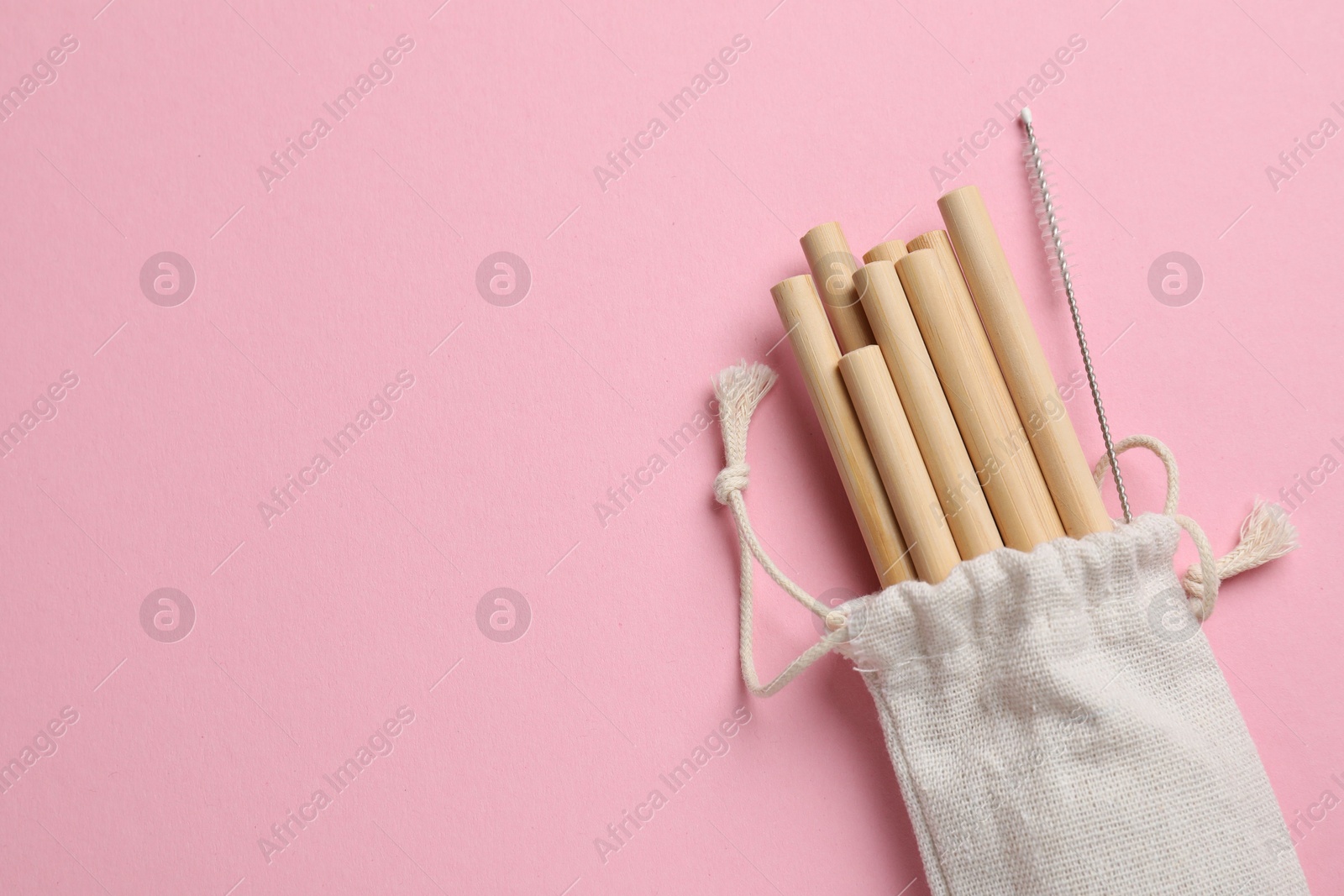 Photo of Bamboo drinking straws and cleaning brush in bag on pink background, top view. Space for text