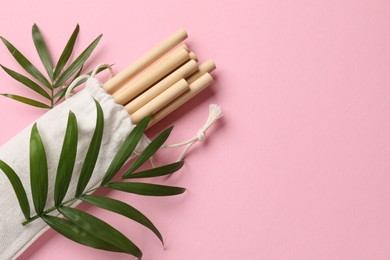 Photo of Bamboo drinking straws in bag and palm leaves on pink background, top view. Space for text