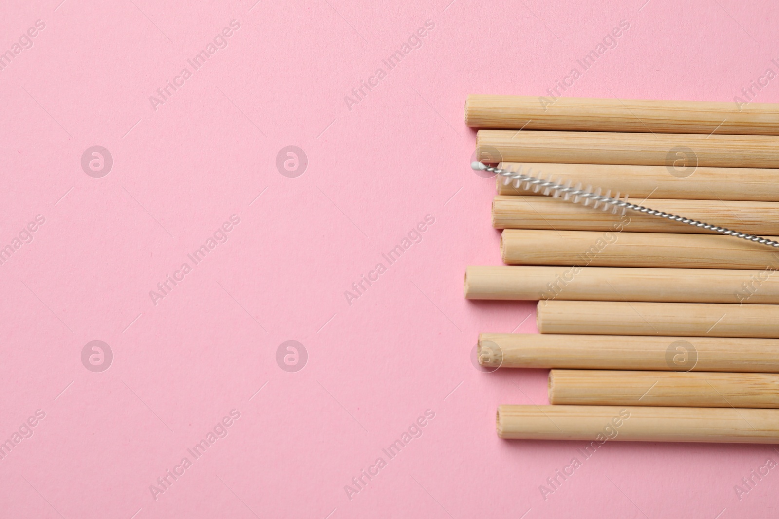 Photo of Bamboo drinking straws and cleaning brush on pink background, top view. Space for text