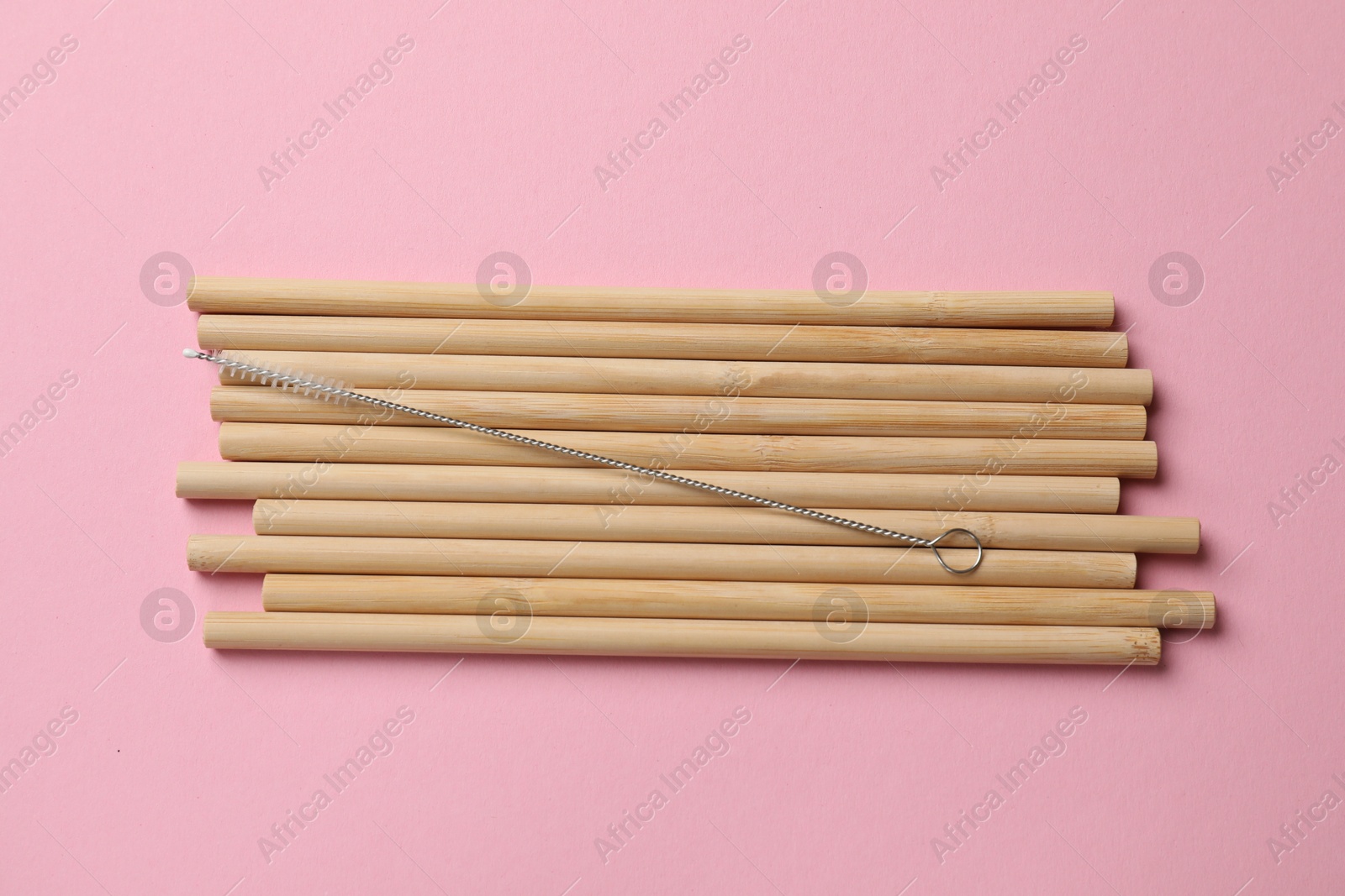 Photo of Bamboo drinking straws and cleaning brush on pink background, top view