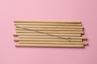 Photo of Bamboo drinking straws and cleaning brush on pink background, top view