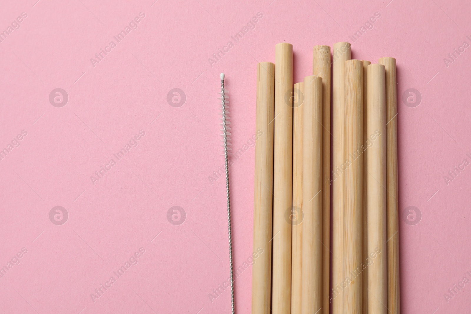 Photo of Bamboo drinking straws and cleaning brush on pink background, top view. Space for text