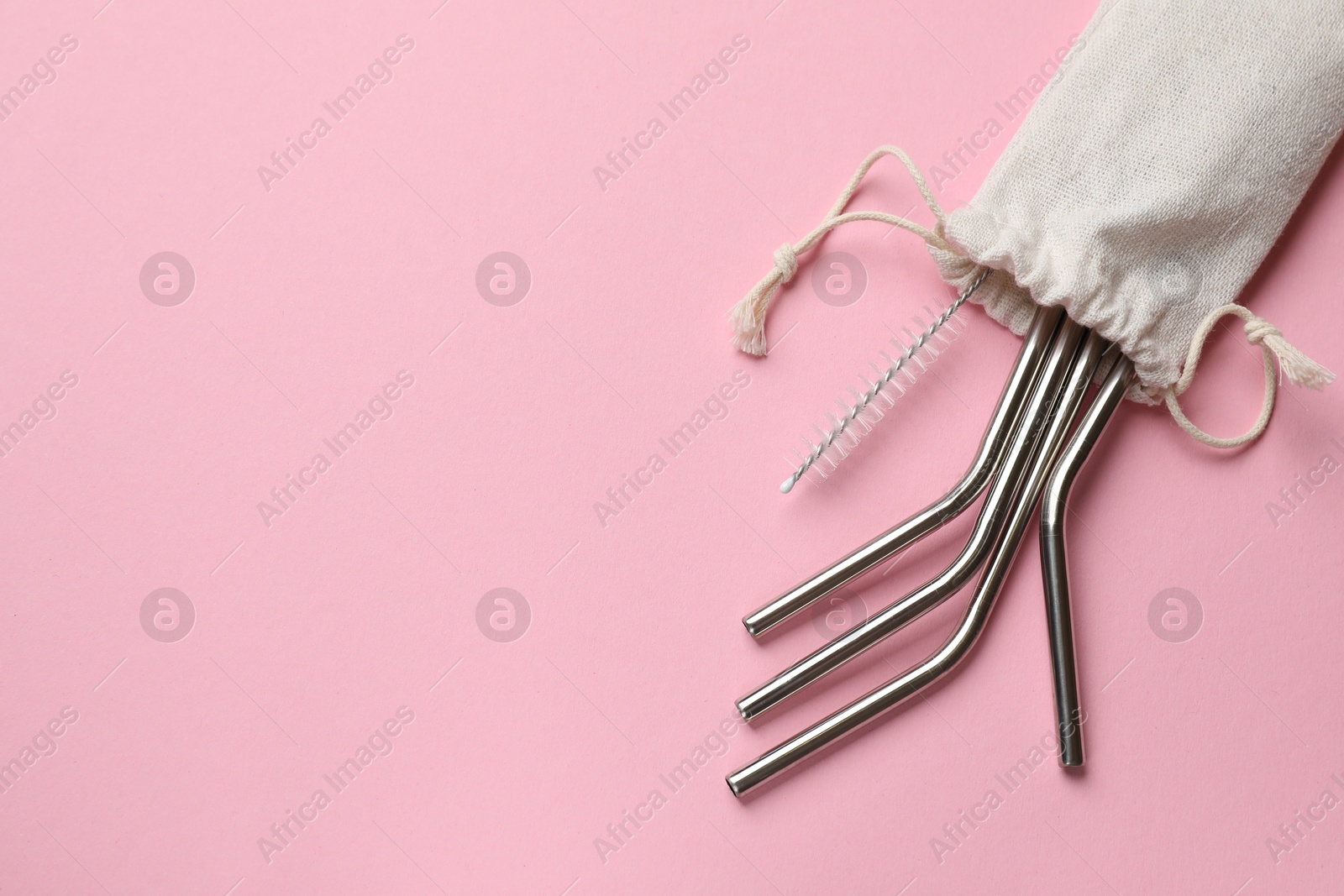 Photo of Metal drinking straws and cleaning brush in bag on pink background, top view. Space for text