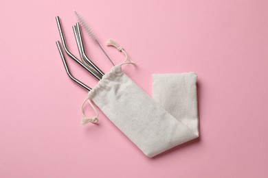 Photo of Metal drinking straws and cleaning brush in bag on pink background, top view