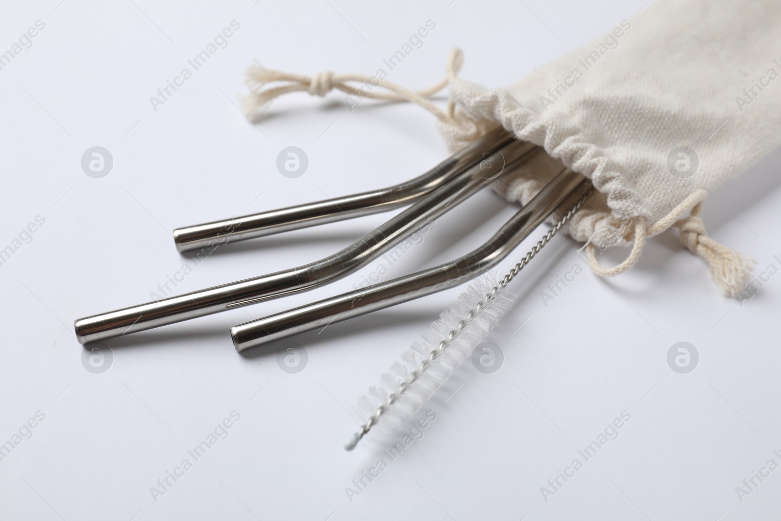 Photo of Metal drinking straws and cleaning brush in bag on white background, closeup