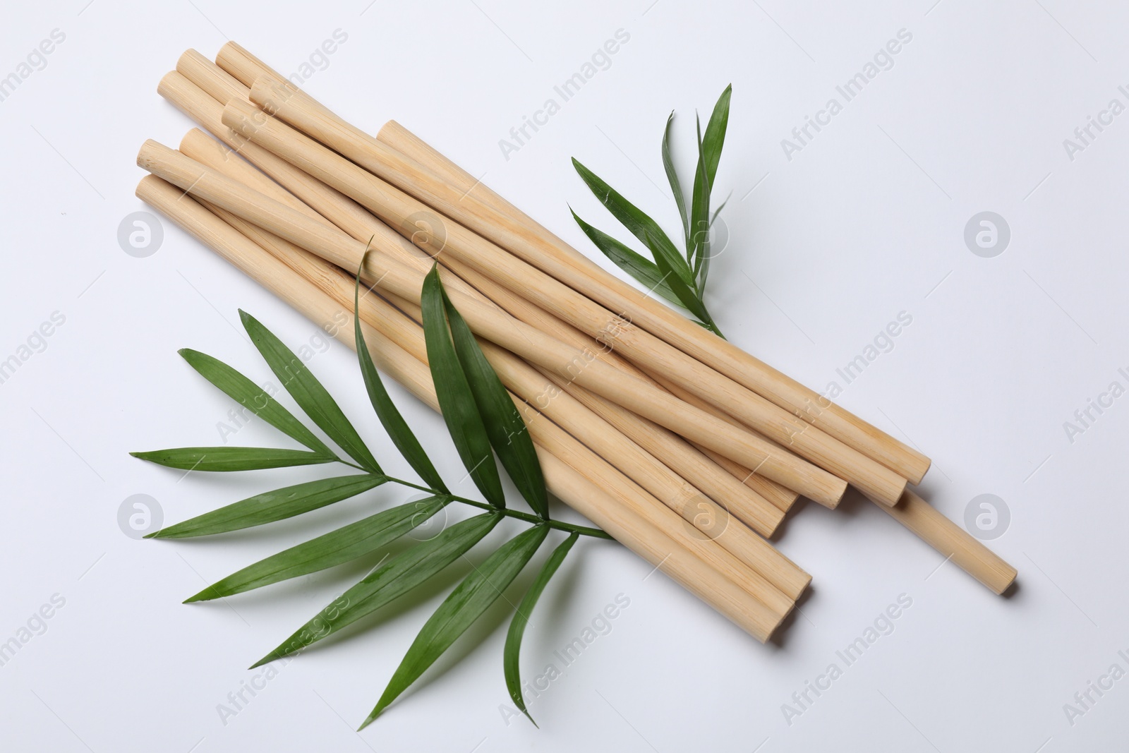 Photo of Bamboo drinking straws and palm leaves on white background, top view