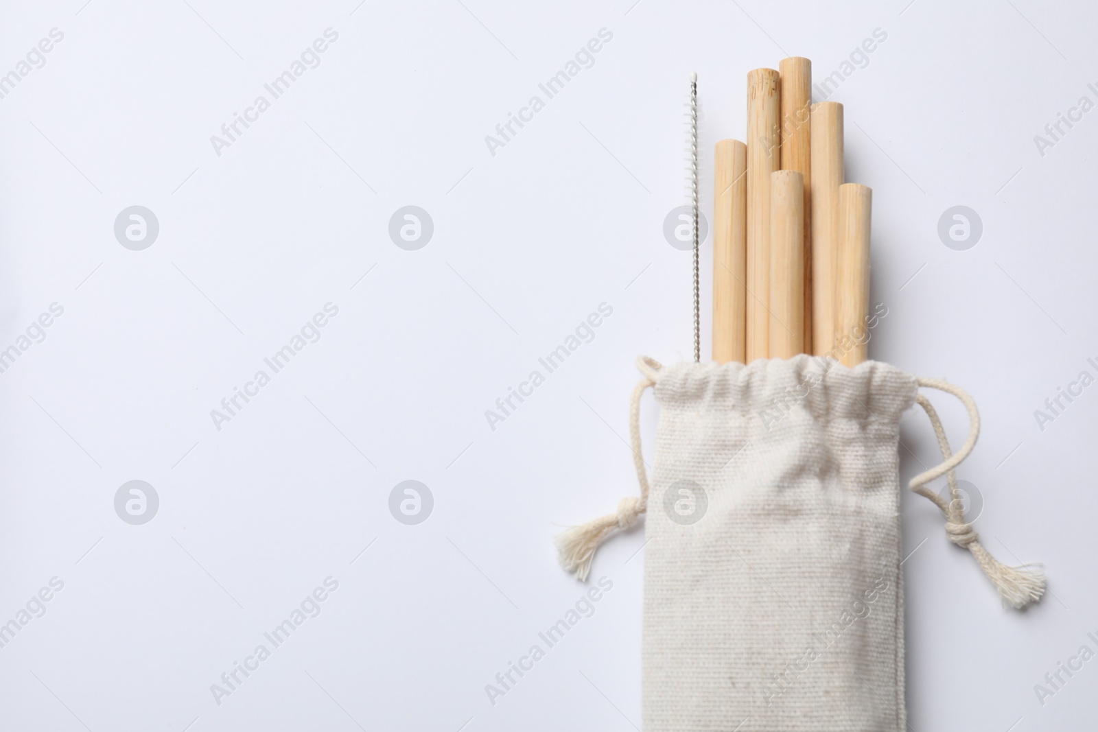 Photo of Bamboo drinking straws and cleaning brush in bag on white background, top view. Space for text